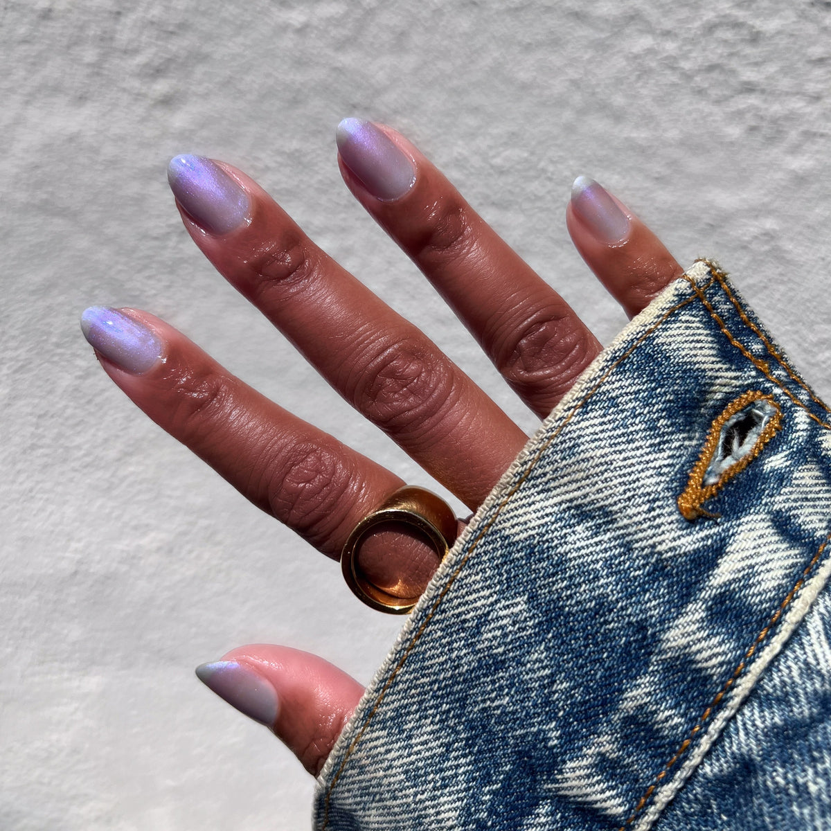 Hand with nails in sheer cool lavender-blue manicure wearing Friend or Anemone? polish and gold ring on denim sleeve